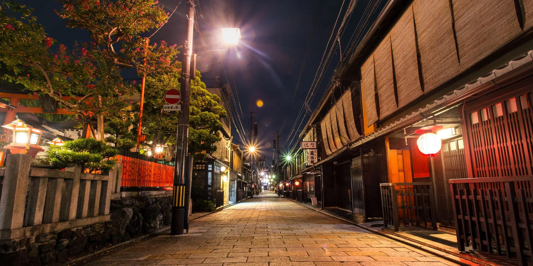 A stone-paved street in Kyoto at night with wooden townhouses and glowing street lamps